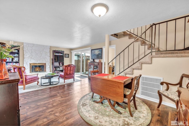 dining room featuring a textured ceiling, dark hardwood / wood-style flooring, and a stone fireplace