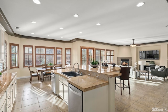 kitchen with dishwasher, white cabinets, sink, an island with sink, and a large fireplace