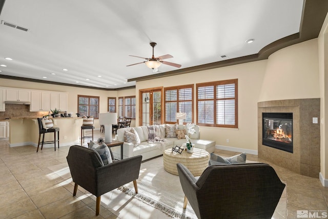 tiled living room with ceiling fan, ornamental molding, and a tiled fireplace