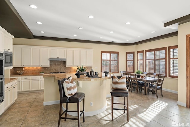 kitchen featuring a center island, white cabinets, a kitchen breakfast bar, crown molding, and decorative backsplash