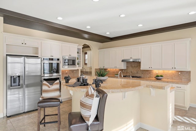 kitchen with white cabinetry, light stone countertops, stainless steel appliances, a breakfast bar area, and a kitchen island with sink