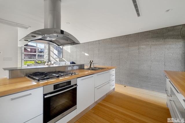 kitchen with sink, butcher block countertops, island range hood, white cabinets, and appliances with stainless steel finishes