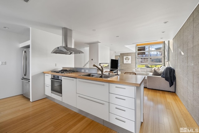 kitchen with sink, kitchen peninsula, wall chimney exhaust hood, white cabinetry, and stainless steel appliances