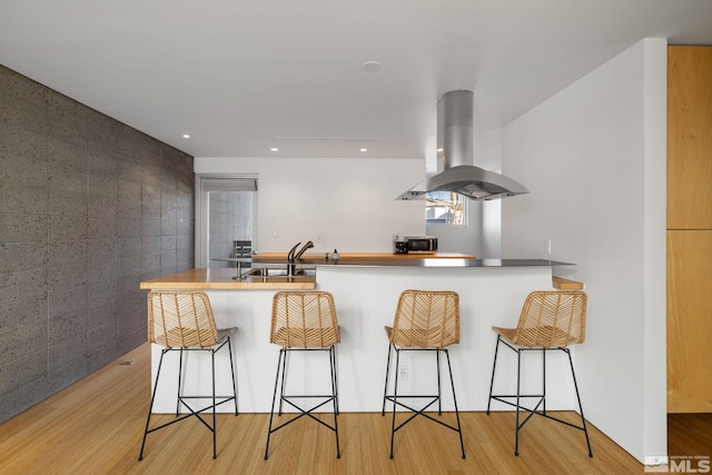 kitchen featuring sink, light hardwood / wood-style flooring, island range hood, kitchen peninsula, and a breakfast bar area