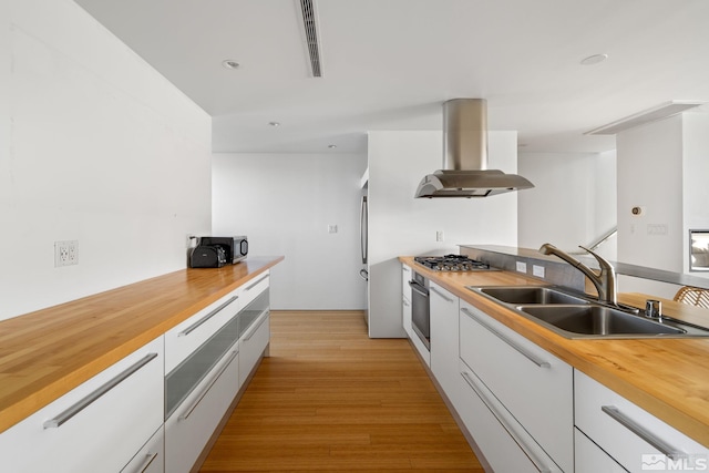 kitchen with white cabinets, ventilation hood, butcher block countertops, and sink