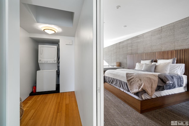 bedroom with stacked washing maching and dryer and hardwood / wood-style flooring