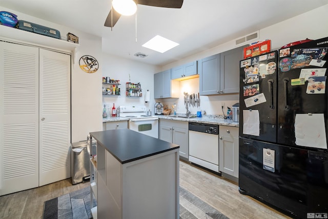 kitchen featuring a skylight, ceiling fan, a center island, white appliances, and light wood-type flooring