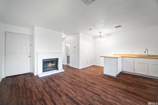 unfurnished living room with a notable chandelier, dark hardwood / wood-style flooring, sink, and a brick fireplace