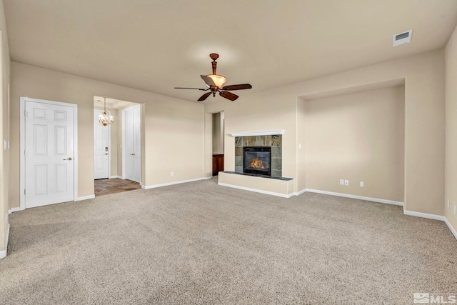 unfurnished living room with a tile fireplace, ceiling fan with notable chandelier, and carpet floors