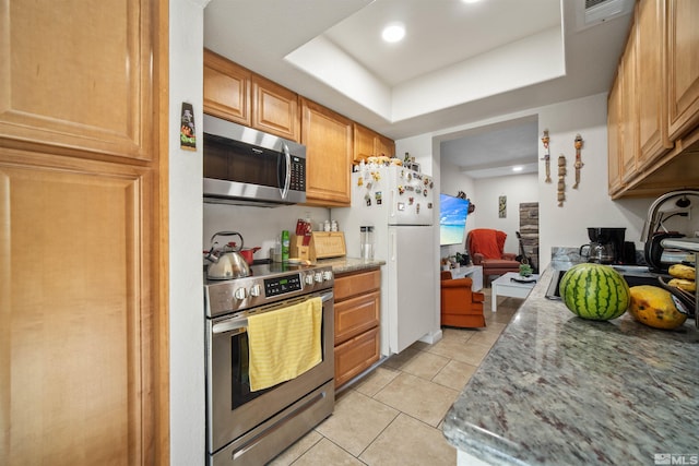 kitchen featuring light tile patterned flooring, light stone counters, appliances with stainless steel finishes, and a tray ceiling