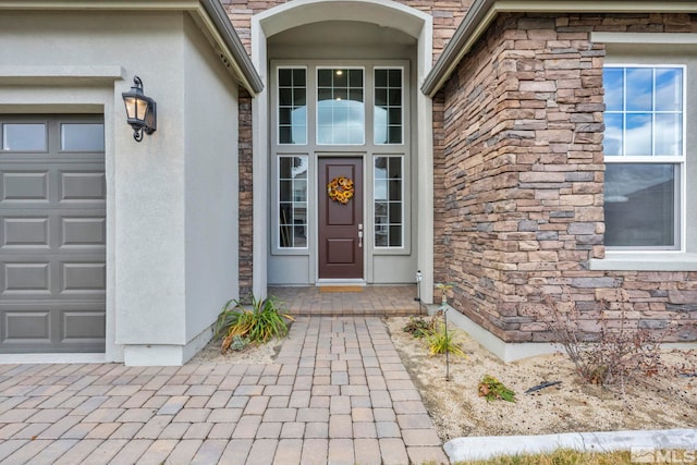 doorway to property featuring stucco siding, stone siding, and an attached garage