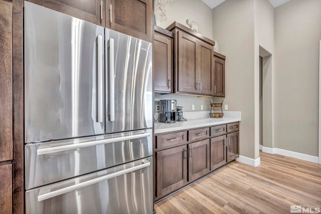 kitchen featuring baseboards, freestanding refrigerator, light countertops, dark brown cabinetry, and light wood-type flooring