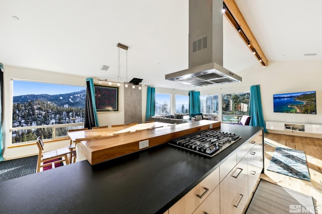 kitchen featuring stainless steel gas cooktop, exhaust hood, wood-type flooring, a mountain view, and vaulted ceiling with beams