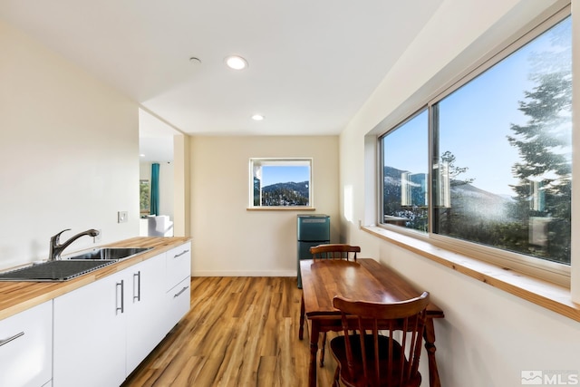 kitchen featuring white cabinets, butcher block counters, sink, and light hardwood / wood-style flooring