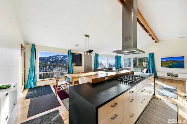 kitchen with vaulted ceiling with beams, island range hood, light wood-type flooring, and stainless steel gas cooktop