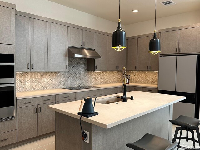 kitchen featuring decorative light fixtures, black electric cooktop, a kitchen island with sink, a breakfast bar, and light tile patterned floors