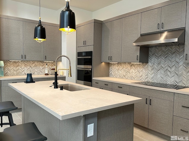 kitchen featuring a breakfast bar, gray cabinets, backsplash, and an island with sink