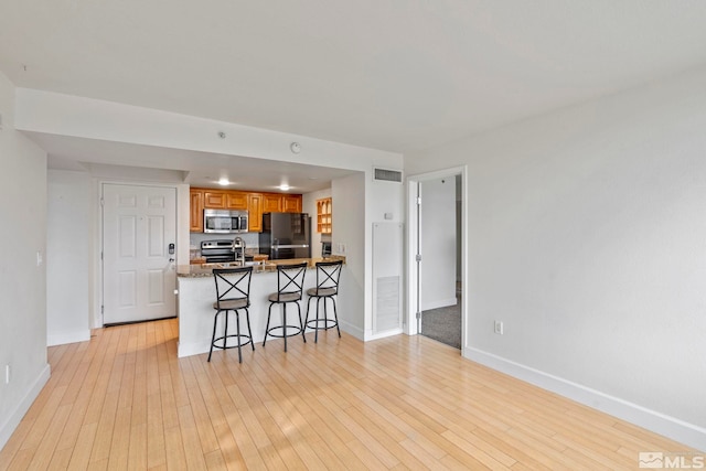 kitchen featuring kitchen peninsula, a breakfast bar, stainless steel appliances, and light hardwood / wood-style flooring