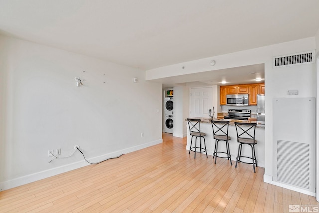 kitchen with stacked washing maching and dryer, stainless steel appliances, kitchen peninsula, a kitchen bar, and light wood-type flooring