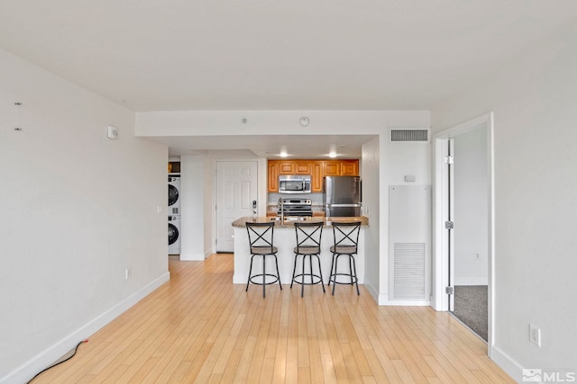 kitchen featuring a breakfast bar area, stacked washer / drying machine, light hardwood / wood-style floors, kitchen peninsula, and stainless steel appliances