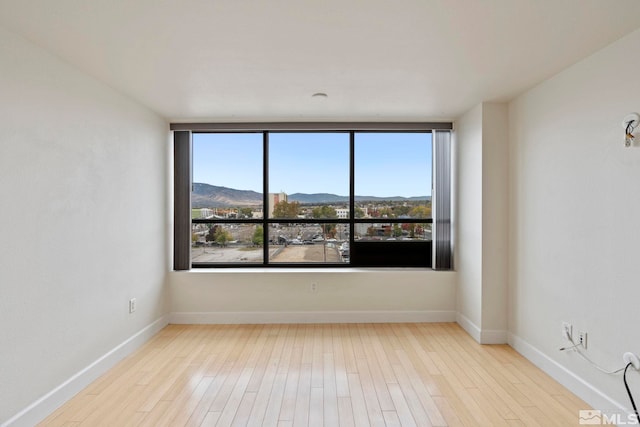 unfurnished room with a mountain view, light wood-type flooring, and a healthy amount of sunlight