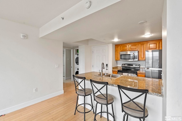 kitchen featuring a kitchen bar, appliances with stainless steel finishes, sink, light hardwood / wood-style flooring, and stacked washer / dryer