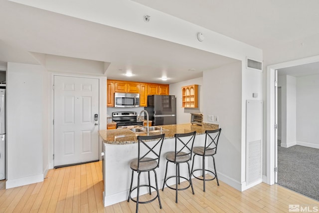 kitchen featuring kitchen peninsula, a kitchen breakfast bar, stainless steel appliances, sink, and stone countertops