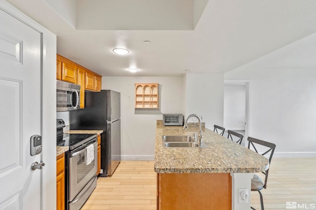 kitchen with light stone countertops, sink, light hardwood / wood-style floors, a breakfast bar area, and appliances with stainless steel finishes