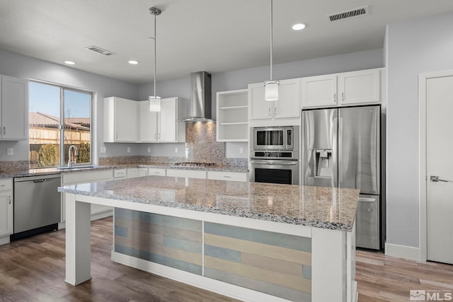 kitchen featuring white cabinetry, wall chimney exhaust hood, hanging light fixtures, stainless steel appliances, and a kitchen island