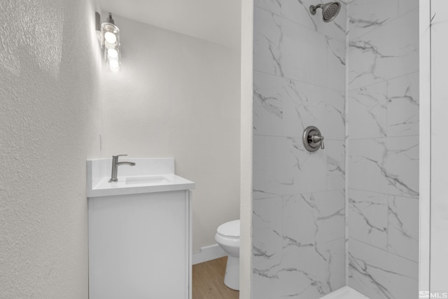 bathroom with hardwood / wood-style floors, vanity, toilet, and a tile shower