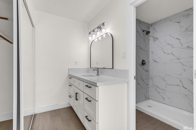 bathroom with a tile shower, vanity, and wood-type flooring