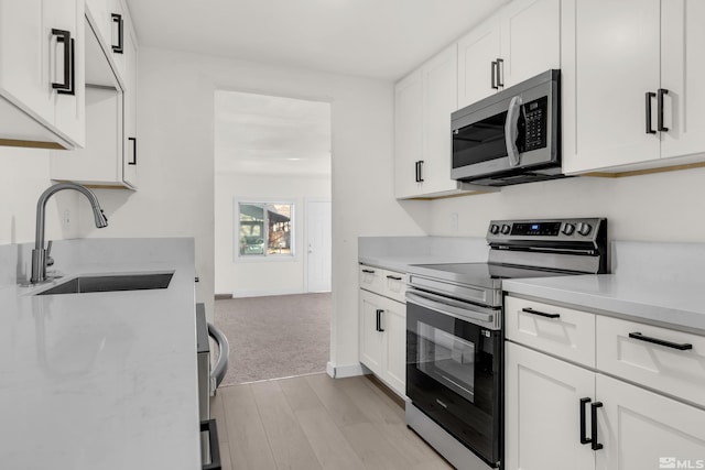 kitchen with light carpet, appliances with stainless steel finishes, white cabinetry, and sink