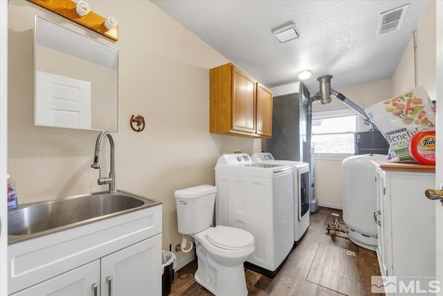 washroom with a textured ceiling, washing machine and dryer, dark wood-type flooring, and sink