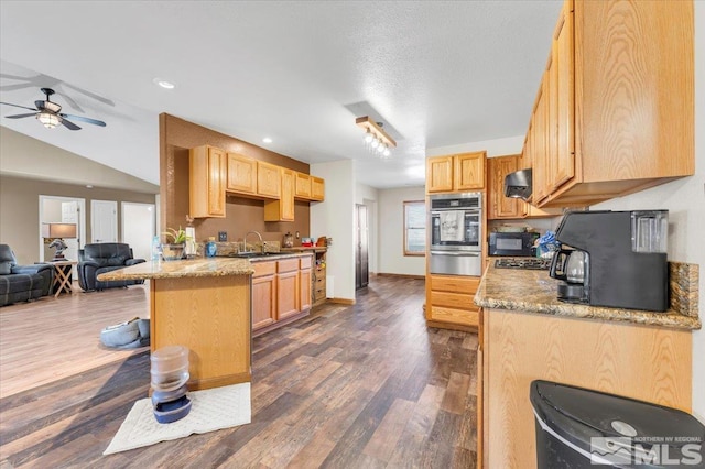 kitchen featuring light brown cabinets, sink, dark hardwood / wood-style floors, oven, and a breakfast bar area