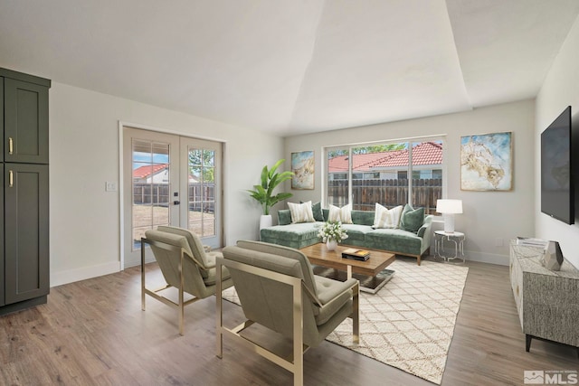 living room with french doors, light hardwood / wood-style floors, and lofted ceiling