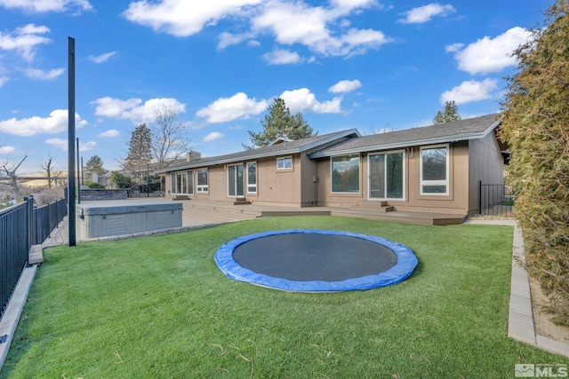 rear view of property with a trampoline and a hot tub