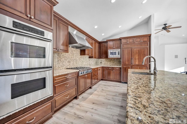 kitchen featuring appliances with stainless steel finishes, tasteful backsplash, light stone counters, vaulted ceiling, and wall chimney range hood