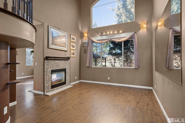 unfurnished living room with a tile fireplace, a high ceiling, and hardwood / wood-style floors