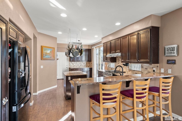 kitchen with decorative backsplash, kitchen peninsula, a breakfast bar, black fridge with ice dispenser, and range