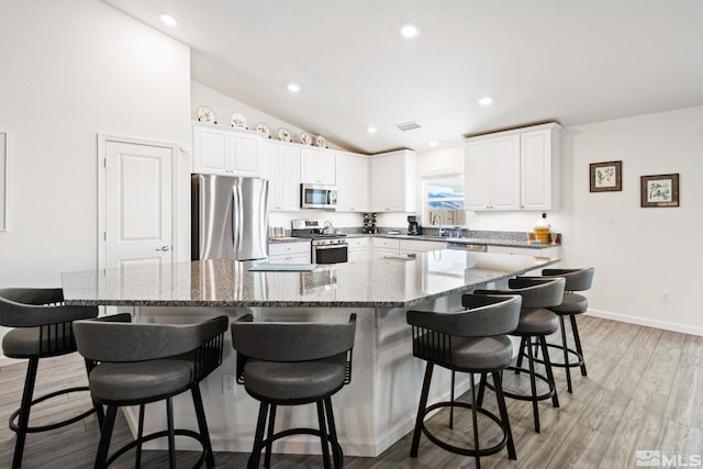 kitchen with dark stone counters, a spacious island, a breakfast bar area, white cabinets, and appliances with stainless steel finishes