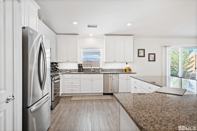 kitchen with appliances with stainless steel finishes, dark stone counters, sink, light hardwood / wood-style flooring, and white cabinets