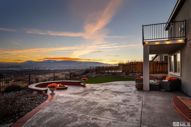 patio terrace at dusk with a mountain view, a balcony, and an outdoor living space