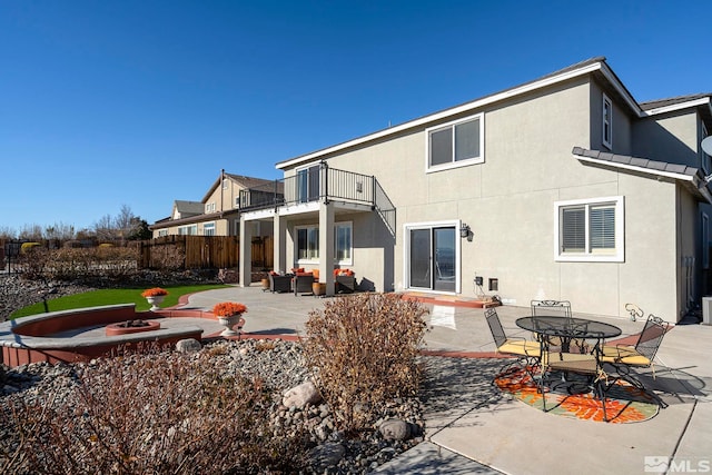 rear view of property featuring a patio area, a balcony, and an outdoor living space with a fire pit