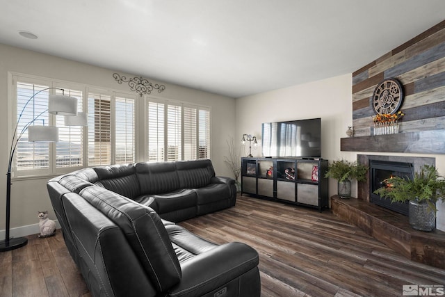 living room with wooden walls, a large fireplace, and dark wood-type flooring