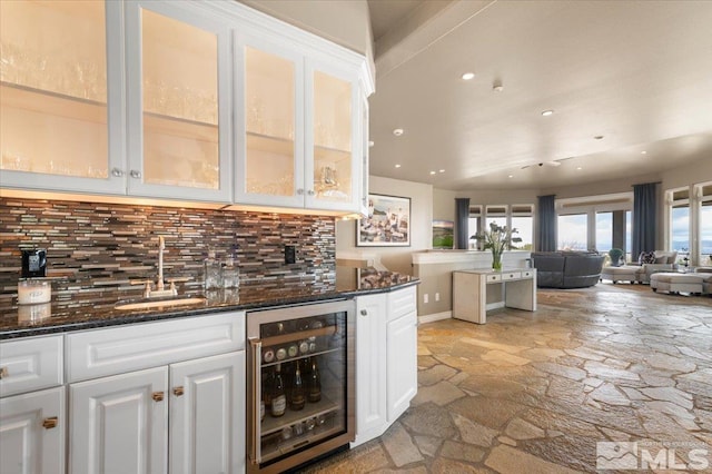 kitchen with white cabinets, decorative backsplash, beverage cooler, and dark stone counters