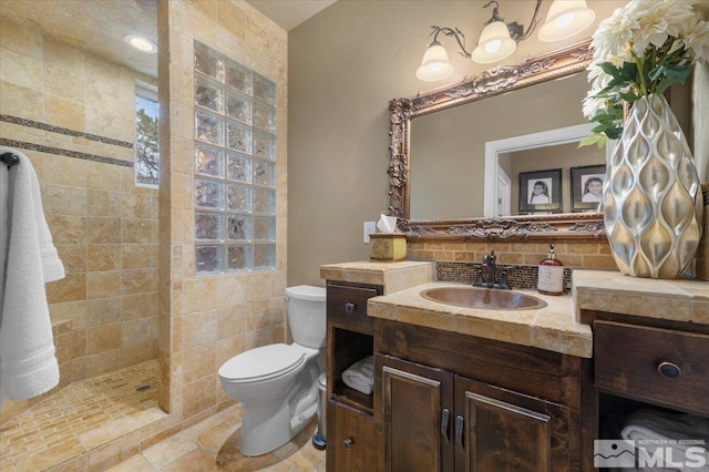 bathroom with vanity, toilet, tiled shower, and tasteful backsplash