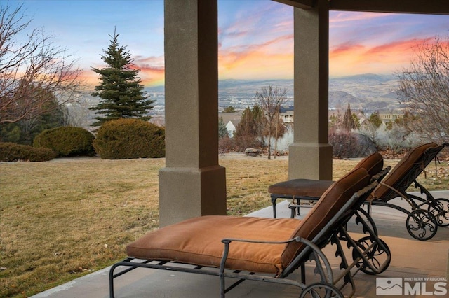 patio terrace at dusk featuring a mountain view and a lawn