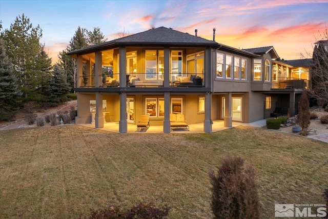 back house at dusk featuring a lawn, a balcony, and a patio