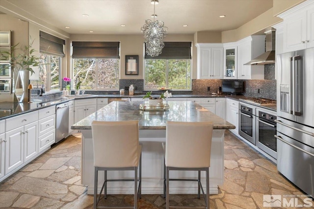 kitchen featuring white cabinets, wall chimney exhaust hood, a center island, and stainless steel appliances