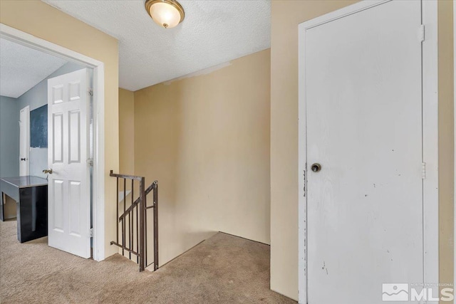 hallway with light carpet and a textured ceiling